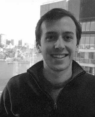 Ben Edelstein in a dark quarter-zip jacket, smiling, with a waterfront skyline behind him